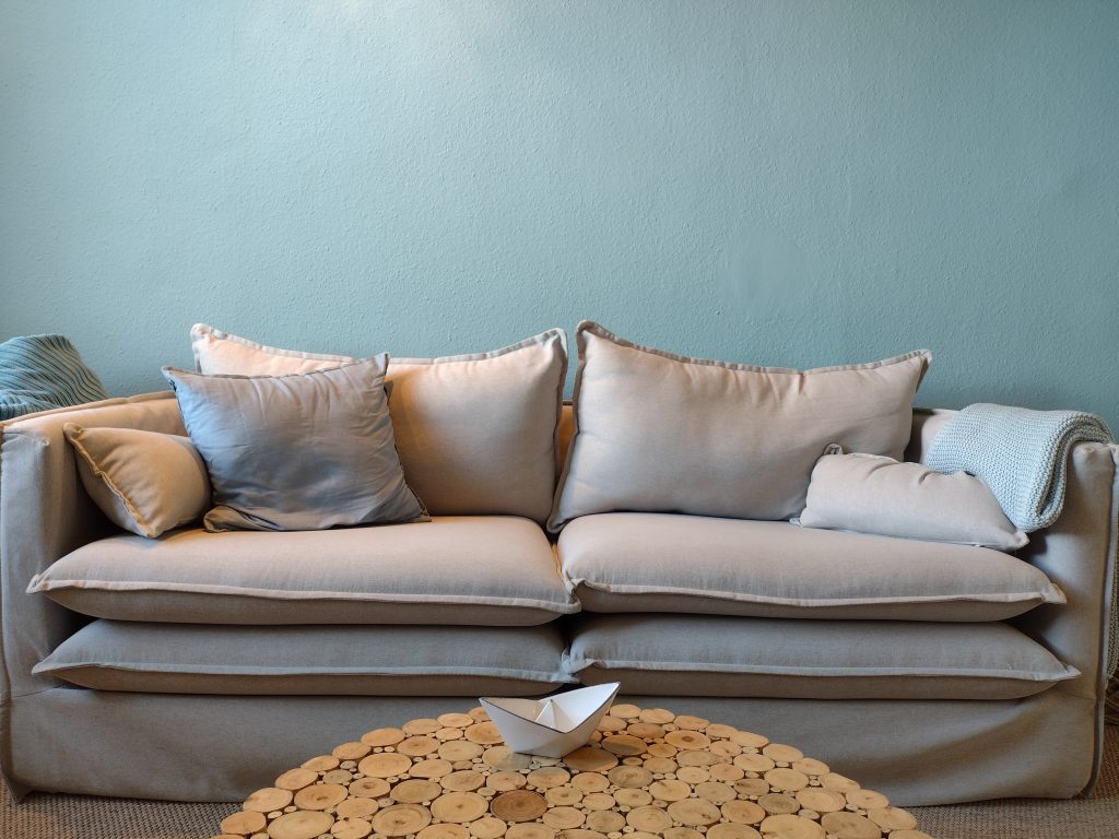 Hellbeiges Sofa mit Kissen, ein runder Couchtisch aus Holz und ein Papierschiffchen als Tafelaufsatz.