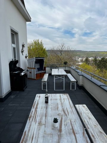 Dachterrasse mit weißen Holztischen, Bänken, Grill und Blick auf die Landschaft.