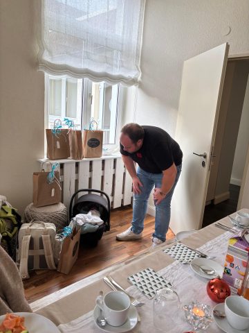 Ein Mann schaut in einen Kindersitz in der Nähe von Geschenktüten in einem für eine Mahlzeit eingerichteten Esszimmer.