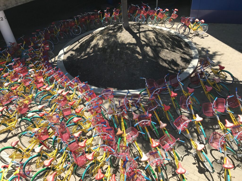 Dutzende bunte Fahrräder sind in einer kreisförmigen Formation um einen kleinen Baum herum geparkt.