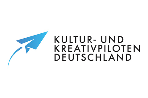 Blaues Papierfliegersymbol mit Text Kultur- und Kreativpiloten Deutschland auf weißem Hintergrund.