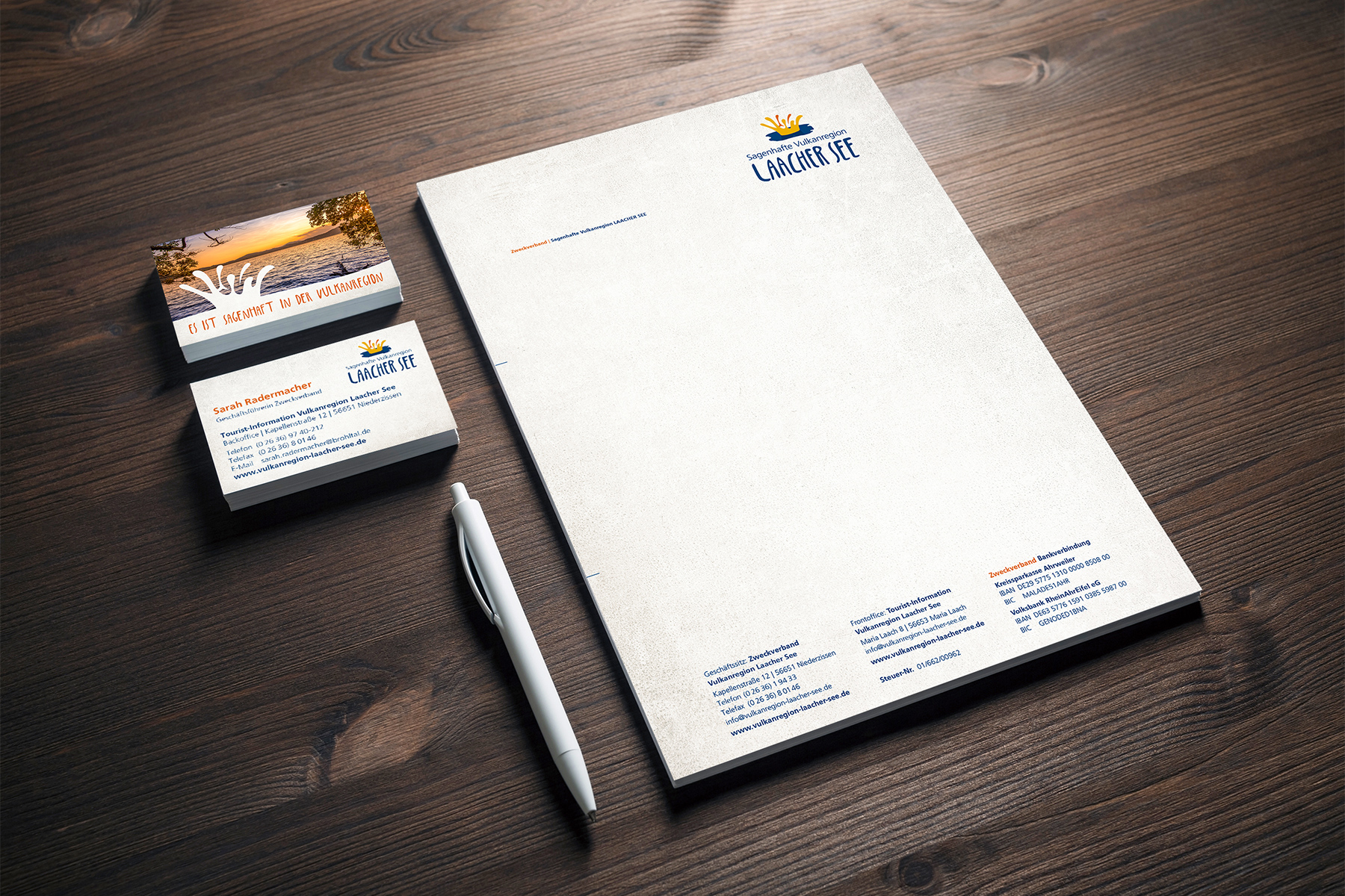 Briefpapier, Visitenkarten und ein Stift auf einem Holztisch mit Larger Life-Branding.