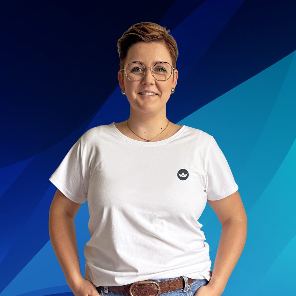 Eine Person mit Brille und weißem T-Shirt steht vor einem blauen geometrischen Hintergrund.
