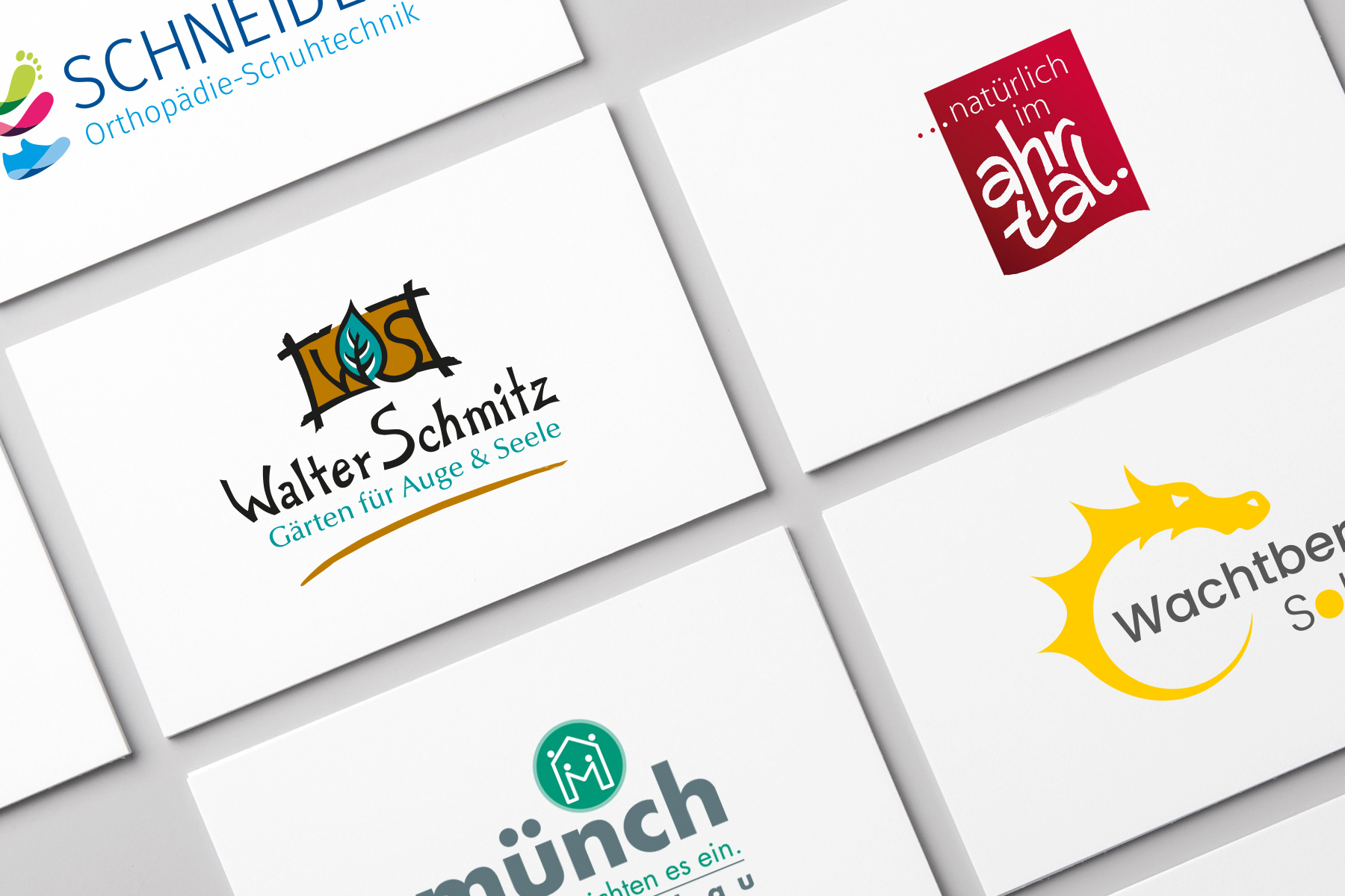 Sechs Visitenkarten mit verschiedenen deutschen Firmenlogos und -designs auf einer flachen Oberfläche.