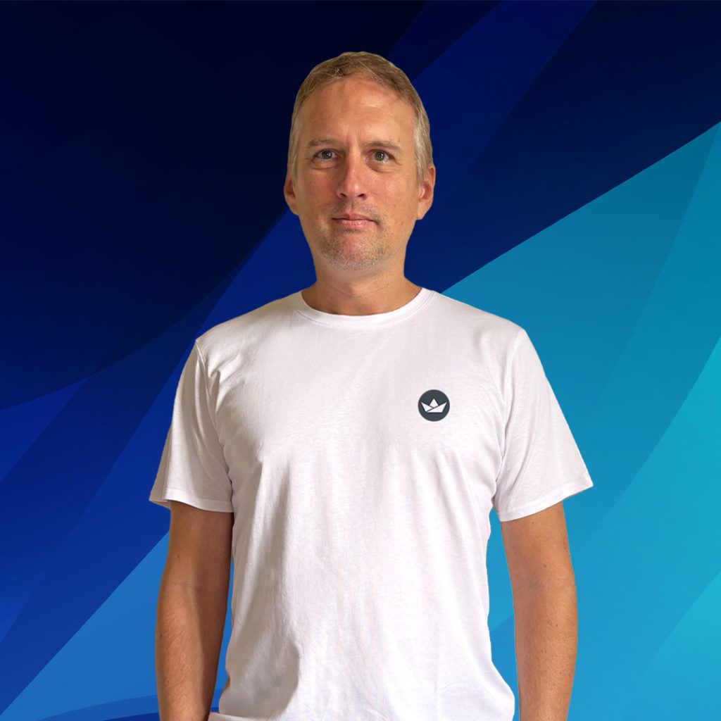 Ein Mann in einem weißen T-Shirt steht vor einem blauen geometrischen Hintergrund.