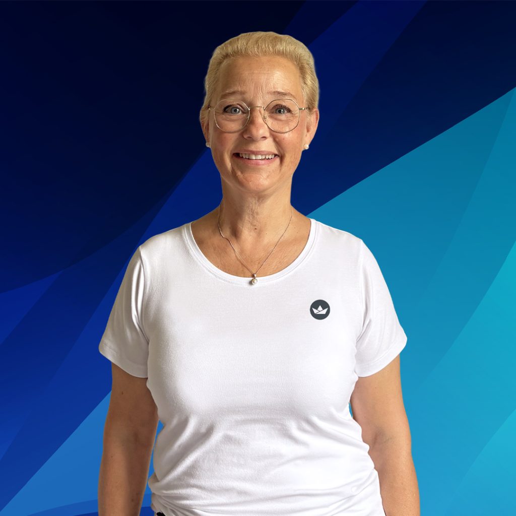Eine lächelnde Frau mit Brille und weißem Hemd steht vor einem blauen, geometrischen Hintergrund.