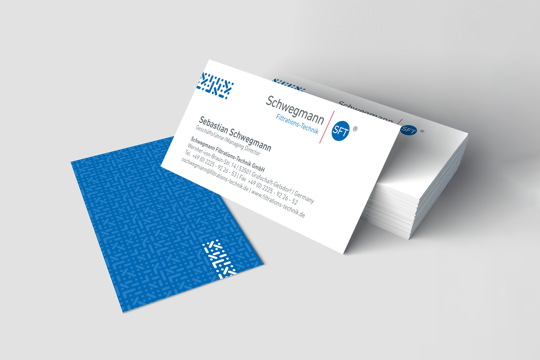 Ein Stapel Visitenkarten mit Kontaktdaten und blauem geometrischen Muster auf der Rückseite.
