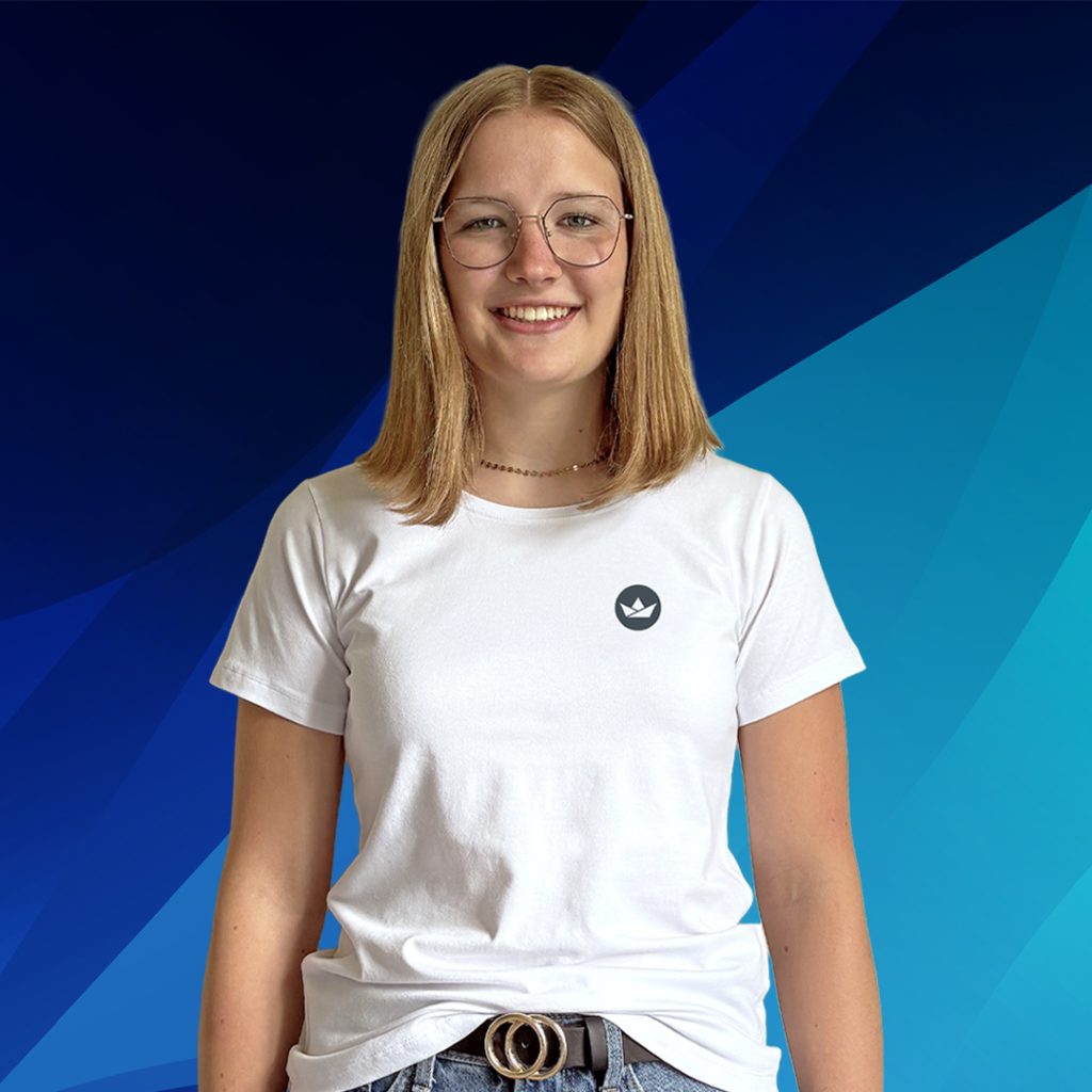 Junge Frau mit Brille, weißem T-Shirt und Jeans steht vor einem blauen geometrischen Hintergrund.