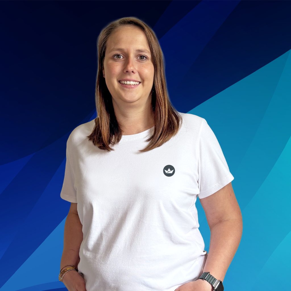 Frau im weißen T-Shirt vor einem blauen geometrischen Hintergrund, Hände in den Taschen.
