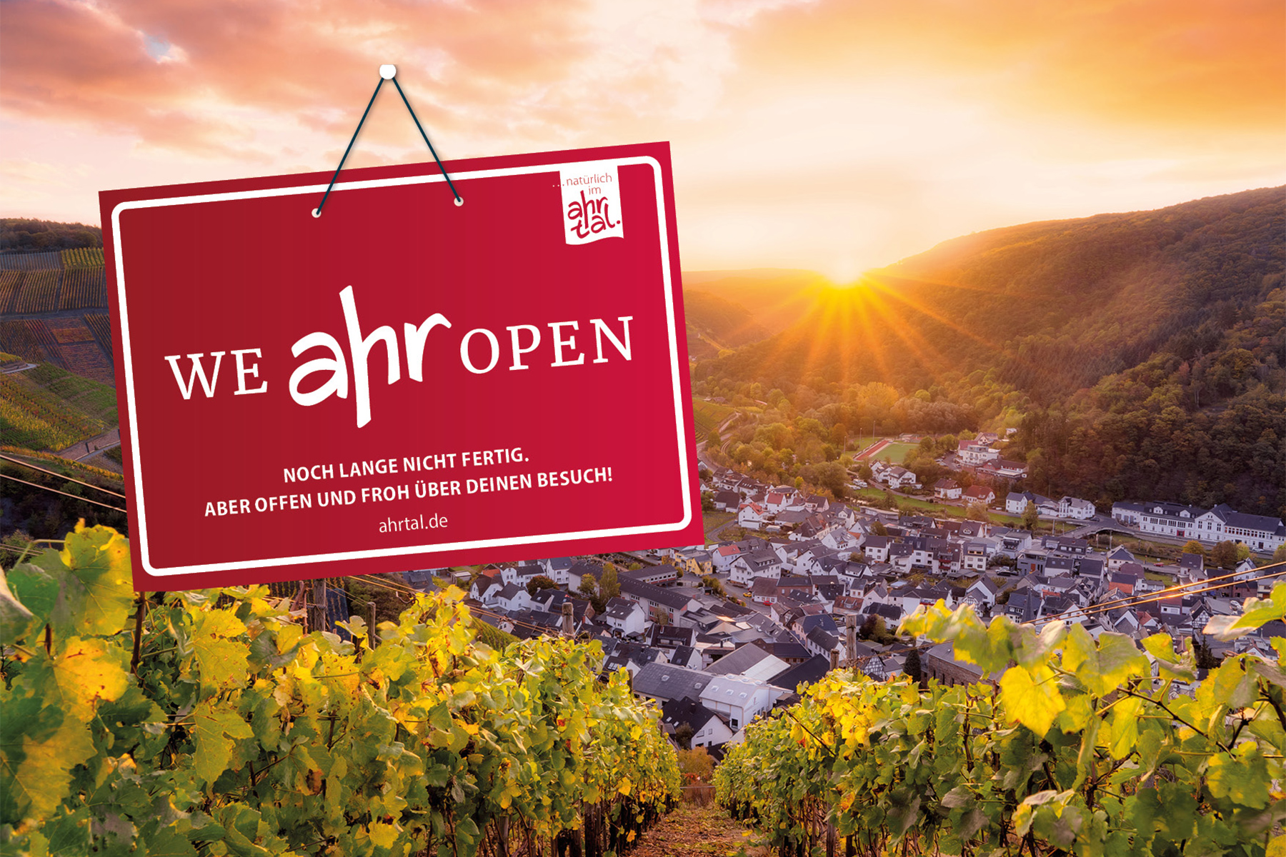 Weinberg über einer Stadt bei Sonnenuntergang mit einem roten Schild mit der Aufschrift We Ahr Open im Vordergrund.