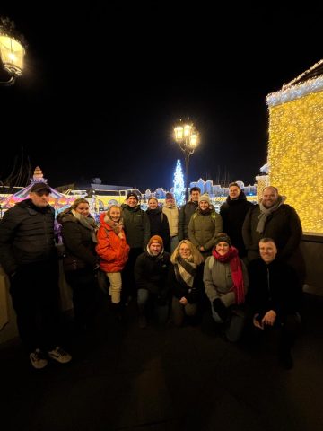 Eine Gruppe von Menschen, die nachts vor festlichen Lichtern und einem beleuchteten Baum zusammen posieren.
