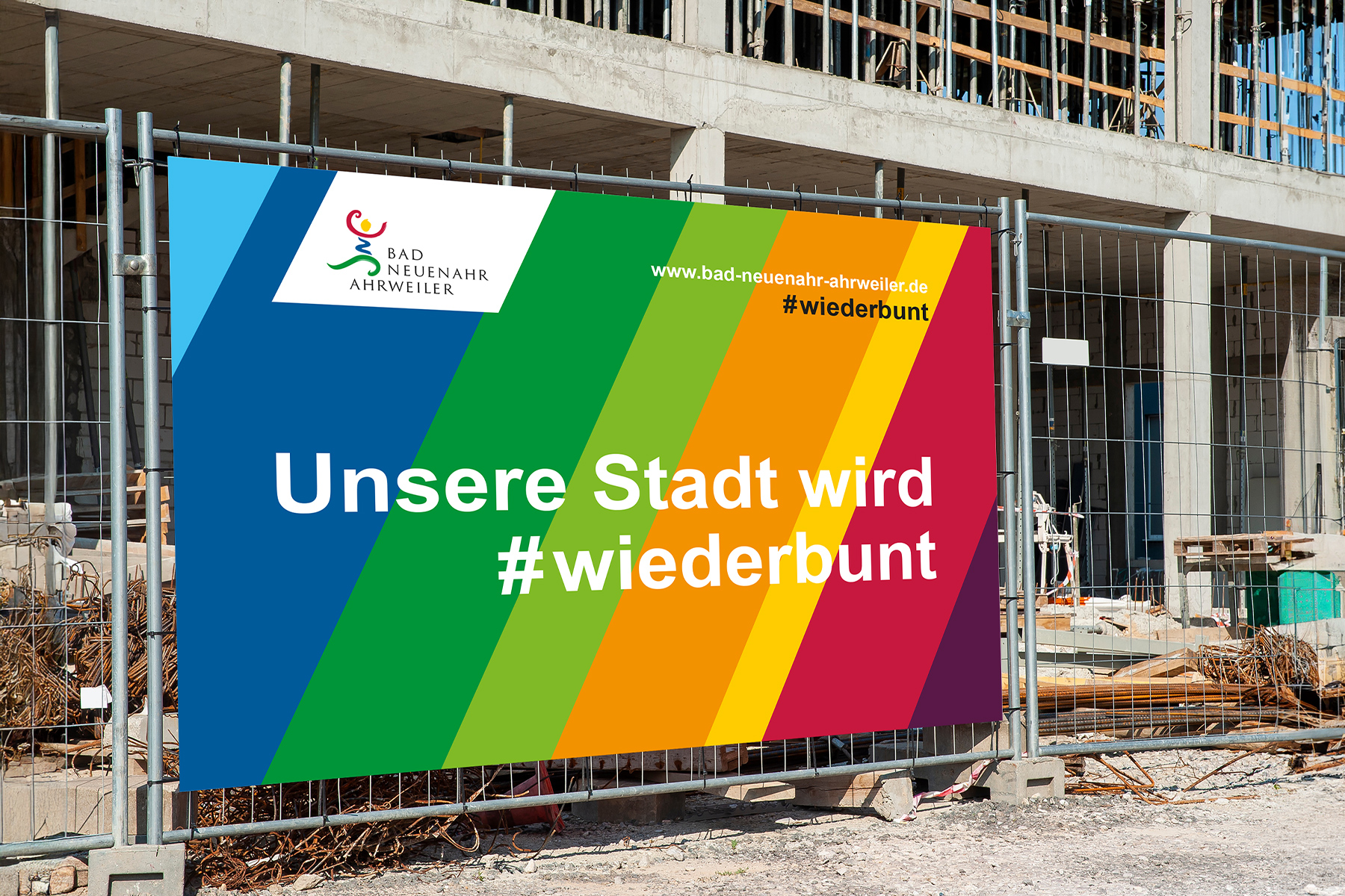 Schild mit Regenbogenstreifen mit der Aufschrift Unsere Stadt wird #wiederbunt an einer Baustelle.