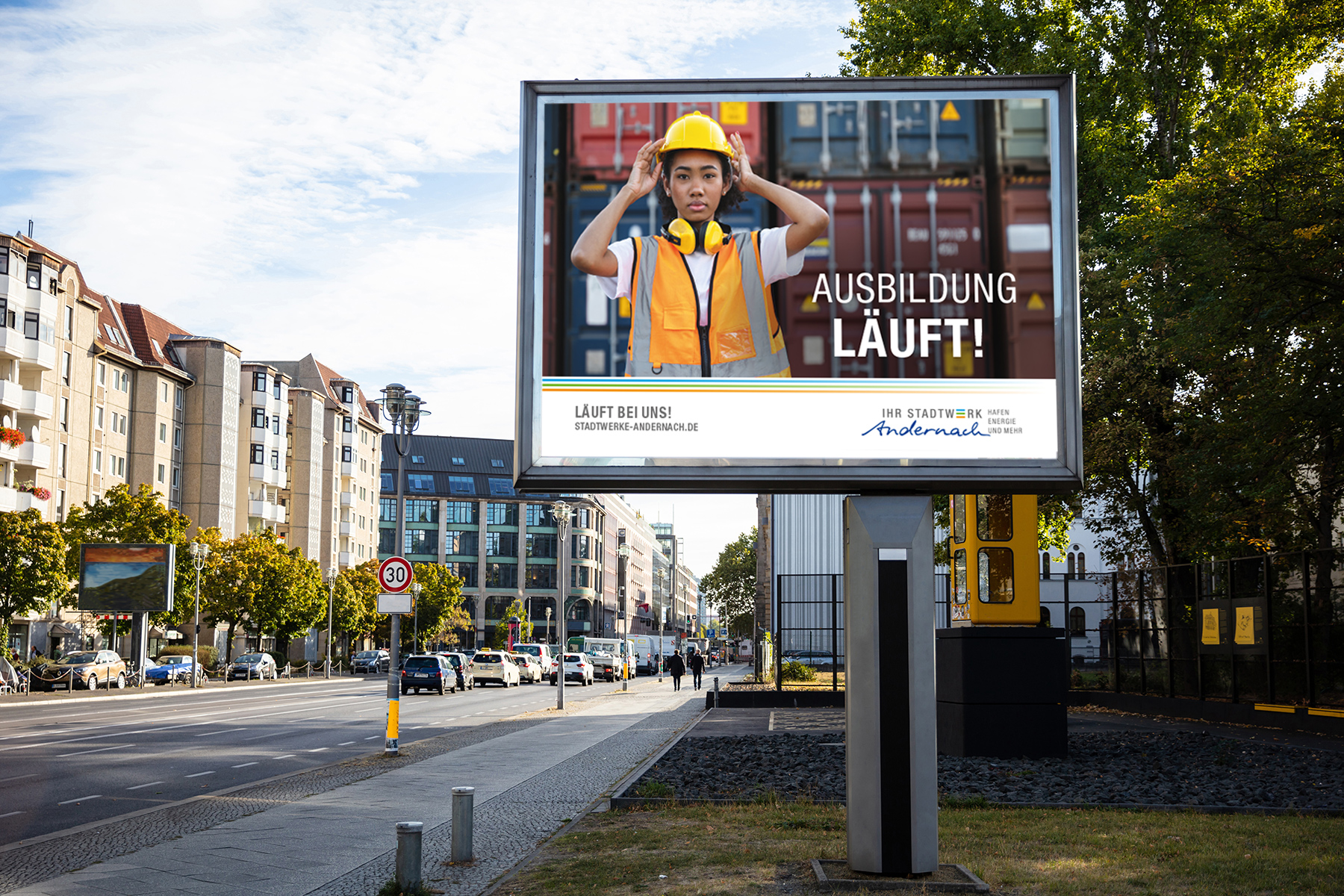 Auf einer Plakatwand ist ein junger Arbeiter in Schutzkleidung zu sehen, begleitet von einem Text, der für eine Berufsausbildung auf Deutsch wirbt.